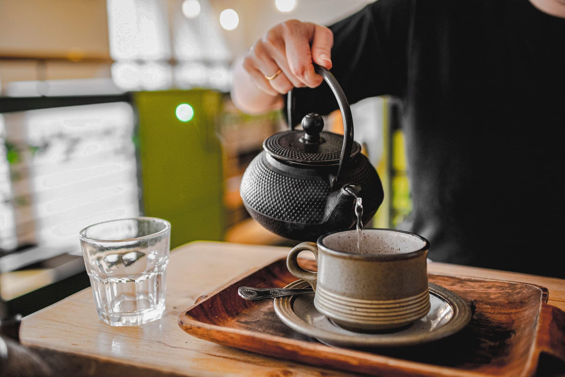 Hot water poured from a kettle into a teapot on a wooden table
